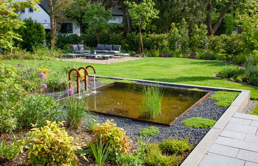 Quadratisches Wasserbecken aus Stahl grenzt an die Terrasse an, umrahmt von einem Beet aus Splitt und Pflanzen