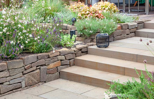 Ein Treppenaufgang mit breiten Stufen führt vom Garten auf die Terrasse, gesäumt von einer Trockenmauer aus Natursteinen