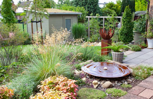 Terrasse und Garten verbindet ein bepflanztes Beet mit dekorativer Wasserschale