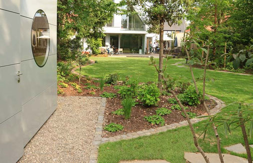 Pflanzbeet mit geschwungener Einfassung aus Naturstein grenzt an das Gartenhaus an