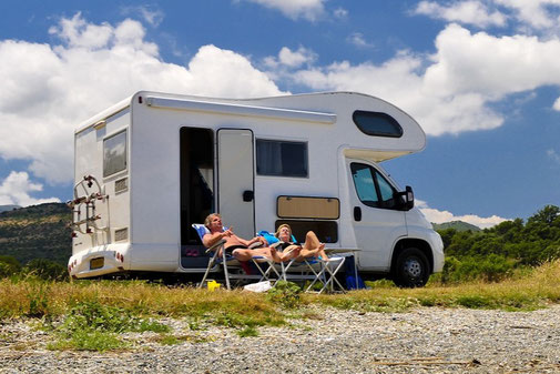 Mann und Frau lümmeln vor dem Womo im Camping-Urlaub mit Wohnmobil-Reiseversicherung der ERGO