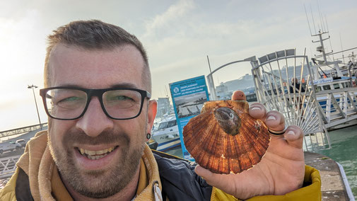 Ein Mann macht ein Selfie im Hafen mit einer Muschelschale.