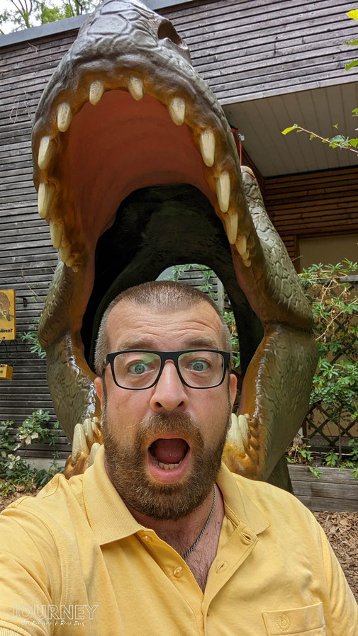 Ein Mann mit offenen Mund steht vor einem Dinosaurierkopf.