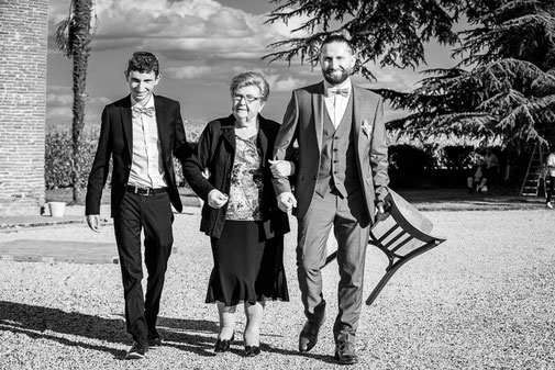 Photographe mariage Montauban – marche bras dessus bras dessous entre une invitée âgée et deux hommes lors d’un mariage