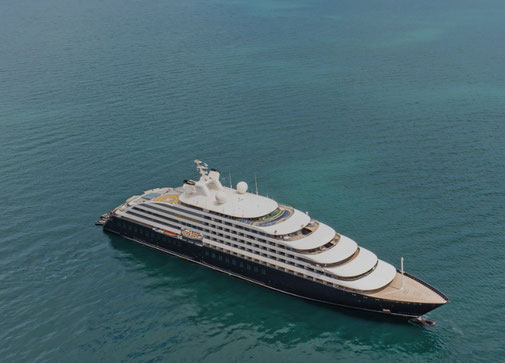 Scenic Eclipse II Yacht liegt im klarem Wasser vor Anker. Im Hintergrund ist eine grüne, felsige Insel