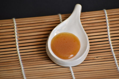 Photo d'une cuillère en céramique blanche d'un Miel de Manuka NPA 24+ de Nouvelle-Zélande sur un support en bambou
