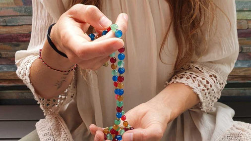 Frau hält eine farbige Mala in beiden Händen und beginnt ihre Meditation. Ideal zur Anleitung für die Anwendung einer Mala.