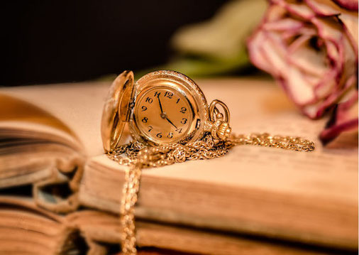 Eine goldene Taschenuhr mit Uhrenkette liegt auf aufgeklappten Büchern