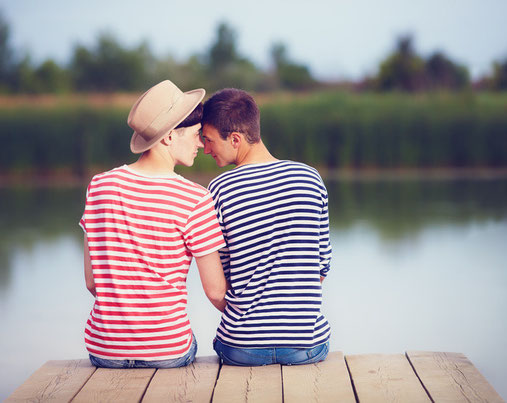 Abgebildet sind zwei Jungs, die glücklich auf einem Steg am See sitzen.