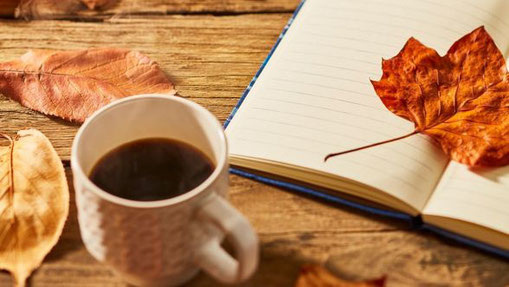 Tasse Kaffee neben geöffnetem Notizbuch und Herbstblättern – Einladung zu Achtsamkeit, Reflexion und Dankbarkeit.