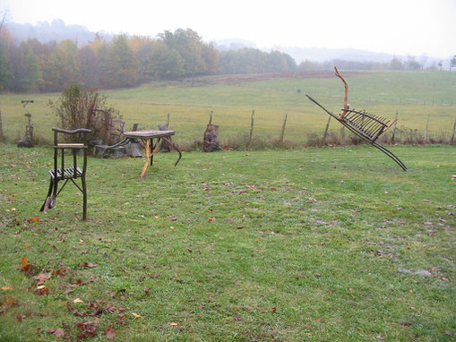 Trois meubles en châtaignier (une chaise, une table, un banc) qui semblent courir car certains de leurs pieds ne touchent pas le sol