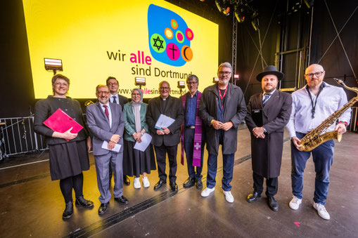 V.l.n.r.  Stv. Superintendentin Leonie Grüning, Imam Ahmad Aweimer, Alexander Krimhand, Prof.Dr. Naciye Kamcili,  Propst Andreas Coersmeier, Pfarrer Friedrich Stiller, OB Thomas Westphal, Rabbiner Avigdor Nosikov, Philipp Sauer (Sax)