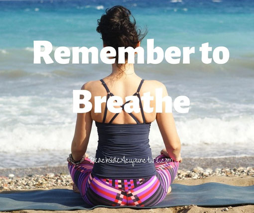 "Remember to breathe" over woman sitting cross-legged on the beach