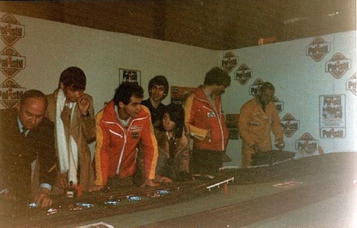 Salon de Bordeaux 1979 le journaliste d'AutoHebdo Eric Bhat avec l'écharpe blanche et les pilotes motul Bertrand Balas et Philippe Streiff autour de la piste de slot racing