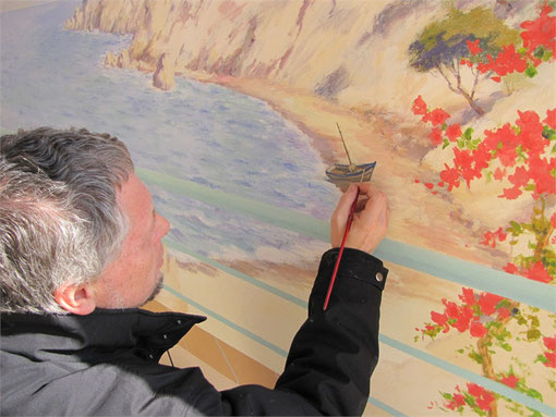 Tony donne le dernier coup de pinceau en plaçant une petite barque sur la plage de la fresque. 