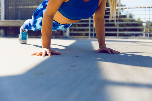 Eine Frau in blauer Sportkleidung macht Liegestütze auf ihrem Balkon.