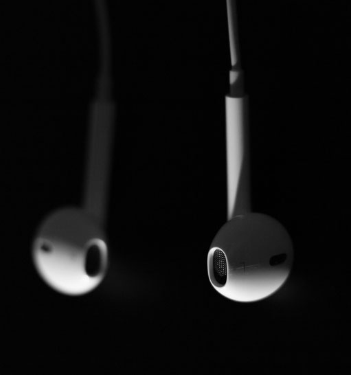 Vor einem schwarzen Hintergrund hängt ein Paar weiße In-Ear-Kopfhörer.