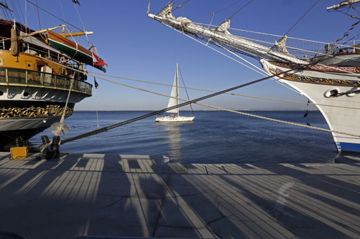 Small wind boat passes between tall ships in Lisbon harbour on July 2016. 