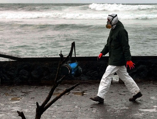 A respirator hangs from fuel oil covered a dead tree as a volunteer passes by at Muxia beach, in the north western Spanish province of Galicia after the oil spilled from the Prestige tanker on December, 2002