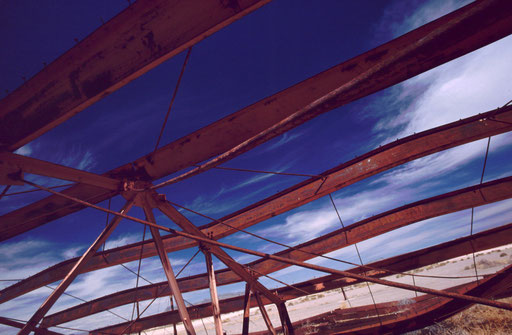The skeletal steel beams of a collapsed building remain where they fell beneath the desert sky. The ruin is a remnant of the 1957 Operation Plumbbob weapons-effects test series.