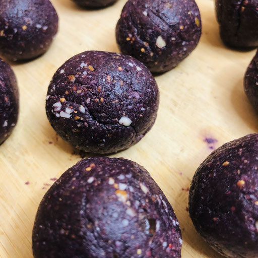 Lila Energyballs auf einem Holzbrett.
