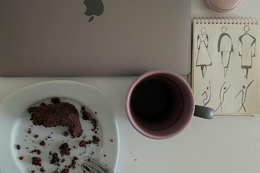 ノートパソコンの前にたべかけのチョコレートケーキのお皿とマグカップ。傍らにメモ帳。