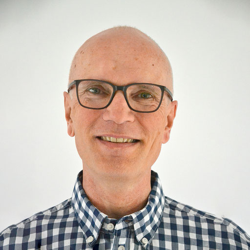 Porträt von Sebastian Lenz aus dem Vorstand des Netzwerk Gewaltfreie Kommunikation Darmstadt. Er hat eine Glatze, trägt ein blaukariertes Hemd und eine Brille mit dunklem Rahmen und lächelt.