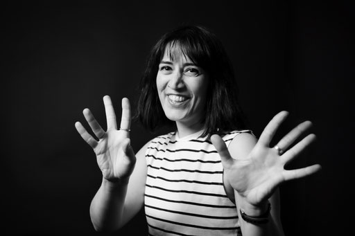 Dunkelhaarige, junge Frau mit gestreiftem Oberteil, lächelnd und mit den Händen gestikulierend. Studio Porträt in Fotostudio Regensburg.