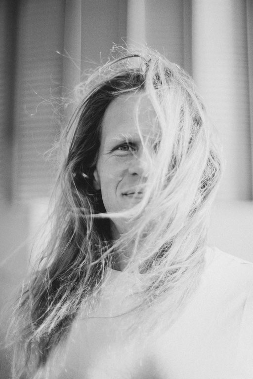 Mann mit wehenden langen Haaren in die Kamera blickend. Schwarz Weiß Porträt Foto aufgenommen von Sebastian Schieder