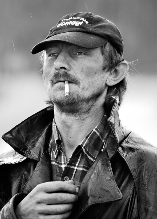 Mann mit Mantel und Zigarette bei Regen, in die Ferne blickend. Aufgenommen von Sebastian Schieder Porträt Fotograf Regensburg.