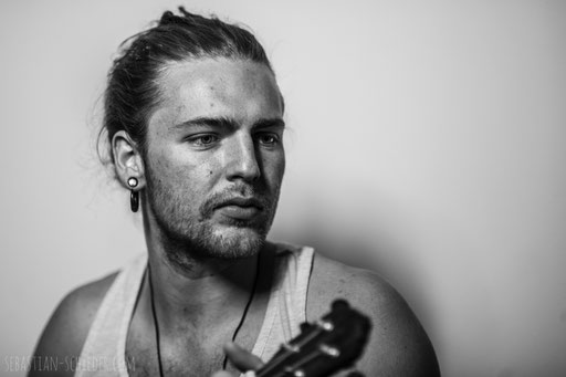 Junger Mann mit langen Haaren und Gitarre, zur Seite blickend. Aufgenommen von Sebastian Schieder Porträt Fotograf Regensburg.