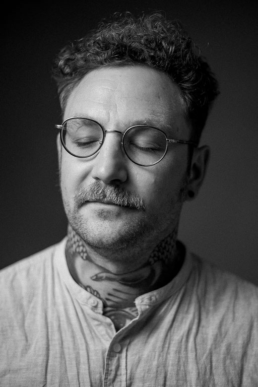 Tätowierter Mann mit Brille und geschlossenen Augen in Fotostudio Beleuchtung. Aufgenommen von Sebastian Schieder Porträt Fotograf Regensburg.