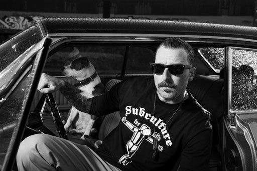 Mann mit dunkler Sonnenbrille in Oldtimer sitzend. Hund auf dem Beifahrersitz. Porträt Foto aufgenommen von Sebastian Schieder
