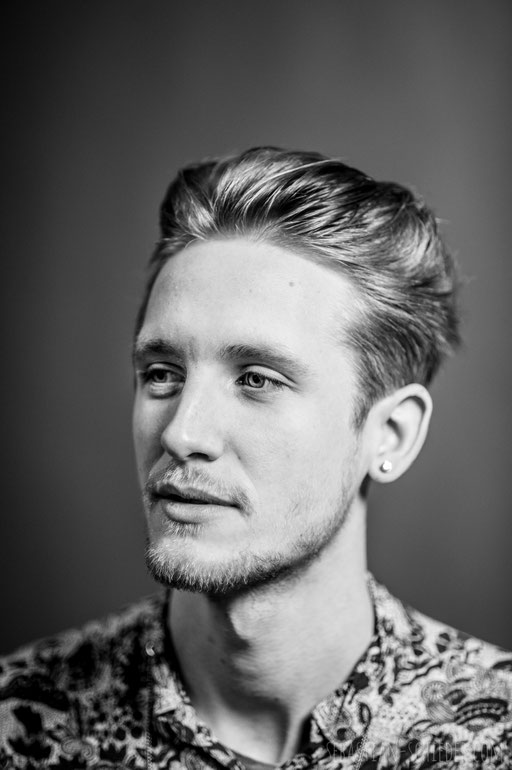 Junger Mann in Studio Beleuchtung vor grauem Hintergrund. Aufgenommen von Sebastian Schieder Porträt Fotograf Regensburg.