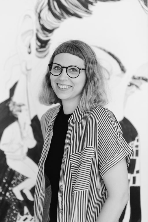 Junge Frau mit Brille vor Kunst Gemälde stehend, lächelnd.