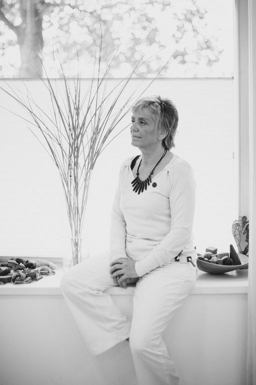 Weiß gekleidete Frau vor einem Fenster sitzend. Aufgenommen von Sebastian Schieder Porträt Fotograf Regensburg.