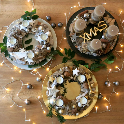 Drei Adventskränze aus haltbaren Hölzern und Rinden in weiß-grau, gold-weiß und braun-gold, mit Lichterkette auf braunem Holztisch dekoriert.