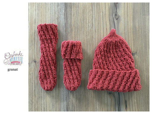 handgestrickte Babyaccessoires - Socken und Mütze in Spiralmuster liegend in granat
