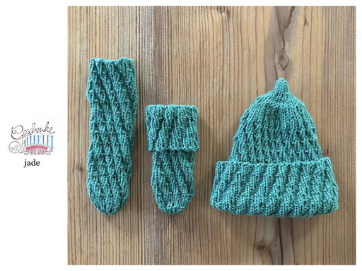 handgestrickte Babyaccessoires - Socken und Mütze in Spiralmuster liegend in jade