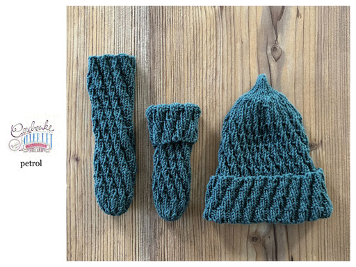 handgestrickte Babyaccessoires - Socken und Mütze in Spiralmuster liegend in petrol