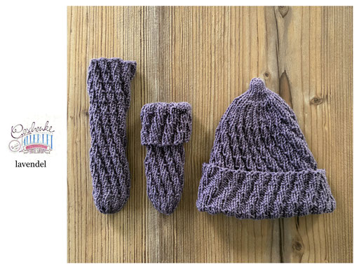 handgestrickte Babyaccessoires - Socken und Mütze in Spiralmuster liegend in lavendel