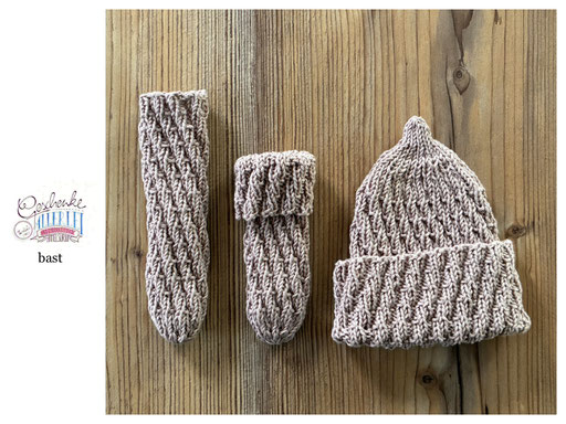 handgestrickte Babyaccessoires - Socken und Mütze in Spiralmuster liegend in bast