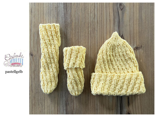 handgestrickte Babyaccessoires - Socken und Mütze in Spiralmuster liegend in pastellgelb