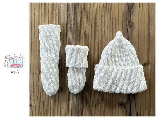 handgestrickte Babyaccessoires - Socken und Mütze in Spiralmuster liegend in weiß