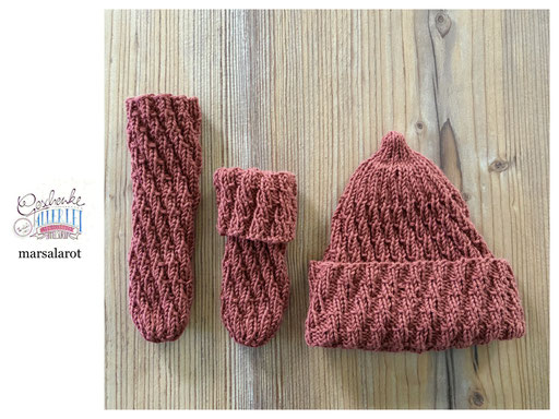 handgestrickte Babyaccessoires - Socken und Mütze in Spiralmuster liegend in marsalarot