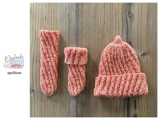 handgestrickte Babyaccessoires - Socken und Mütze in Spiralmuster liegend in aprikose