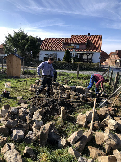 Verteilt liegende Steine, die zu einer Mauer aufgeschichtet werden