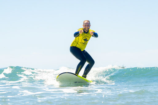 Beginner surfer standing up on a small wave during surf lesson in Gran Canaria.