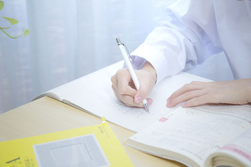 机でノートに書き込みをする高校生の姿。参考書や問題集を広げ、定期テストと入試対策を両立させている学習風景。