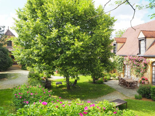 Terrasse fleurie de la maison d'hôtes La Lysiane avec salon de jardin sous le tilleul pour le petit-déjeuner.